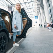 Calm stylish female passenger getting out of taxi parked before airport terminal building